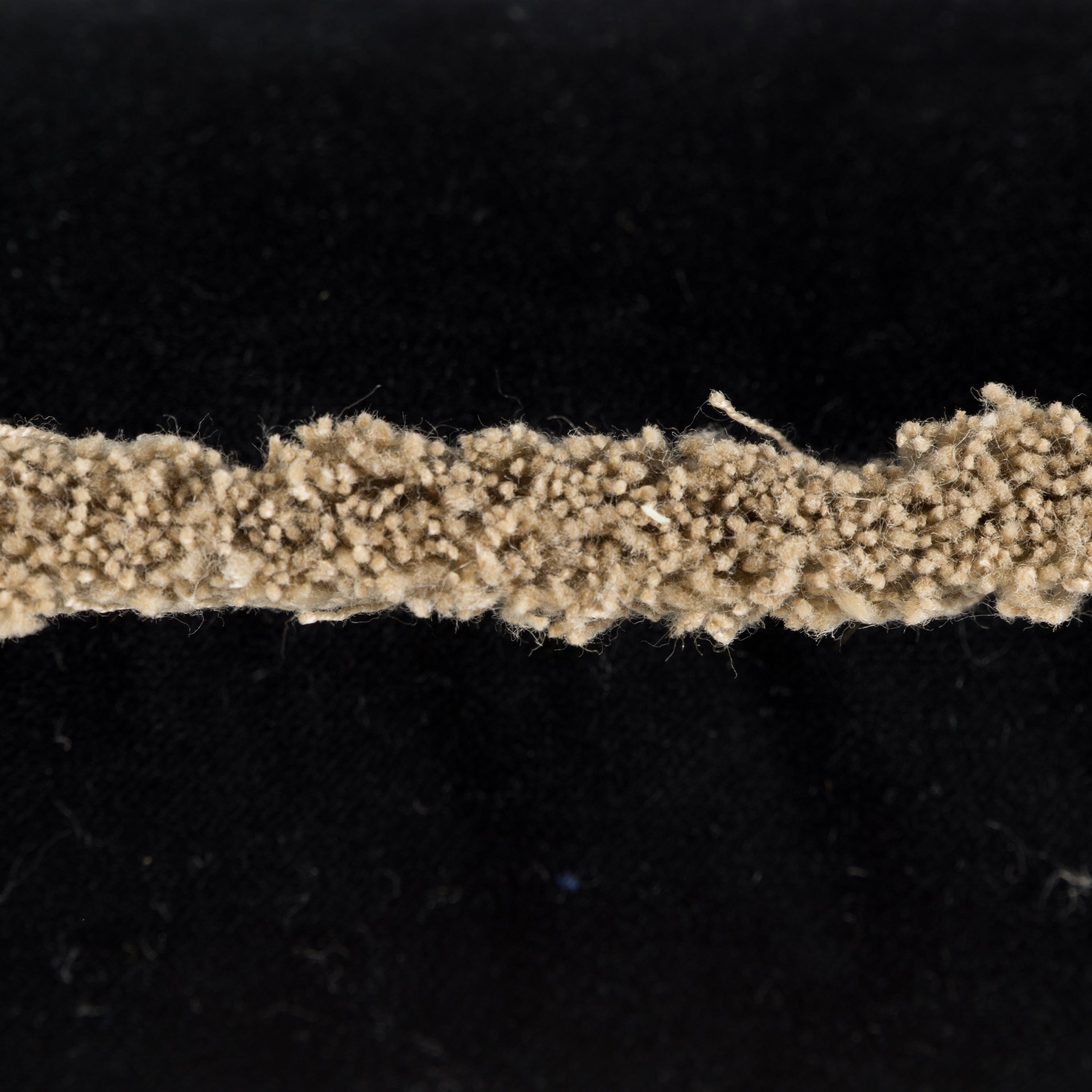 Close-up of beige textured fabric strip on a black velvet cushion