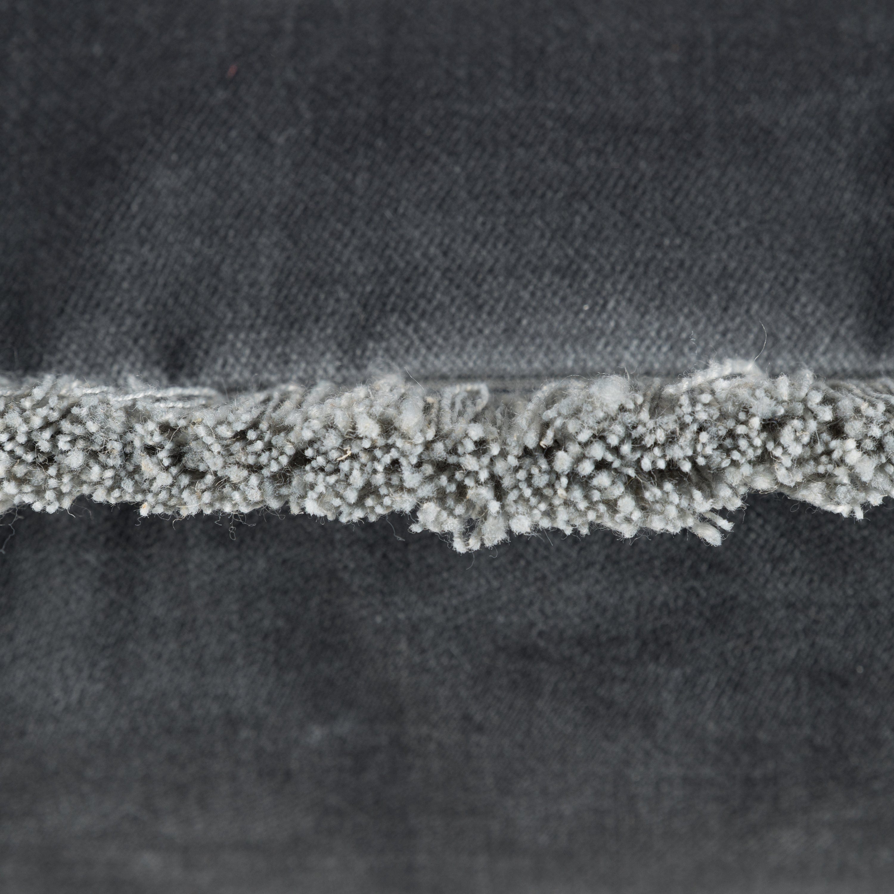 Close-up of a textured tassel fabric edge on a slate blue cushion background