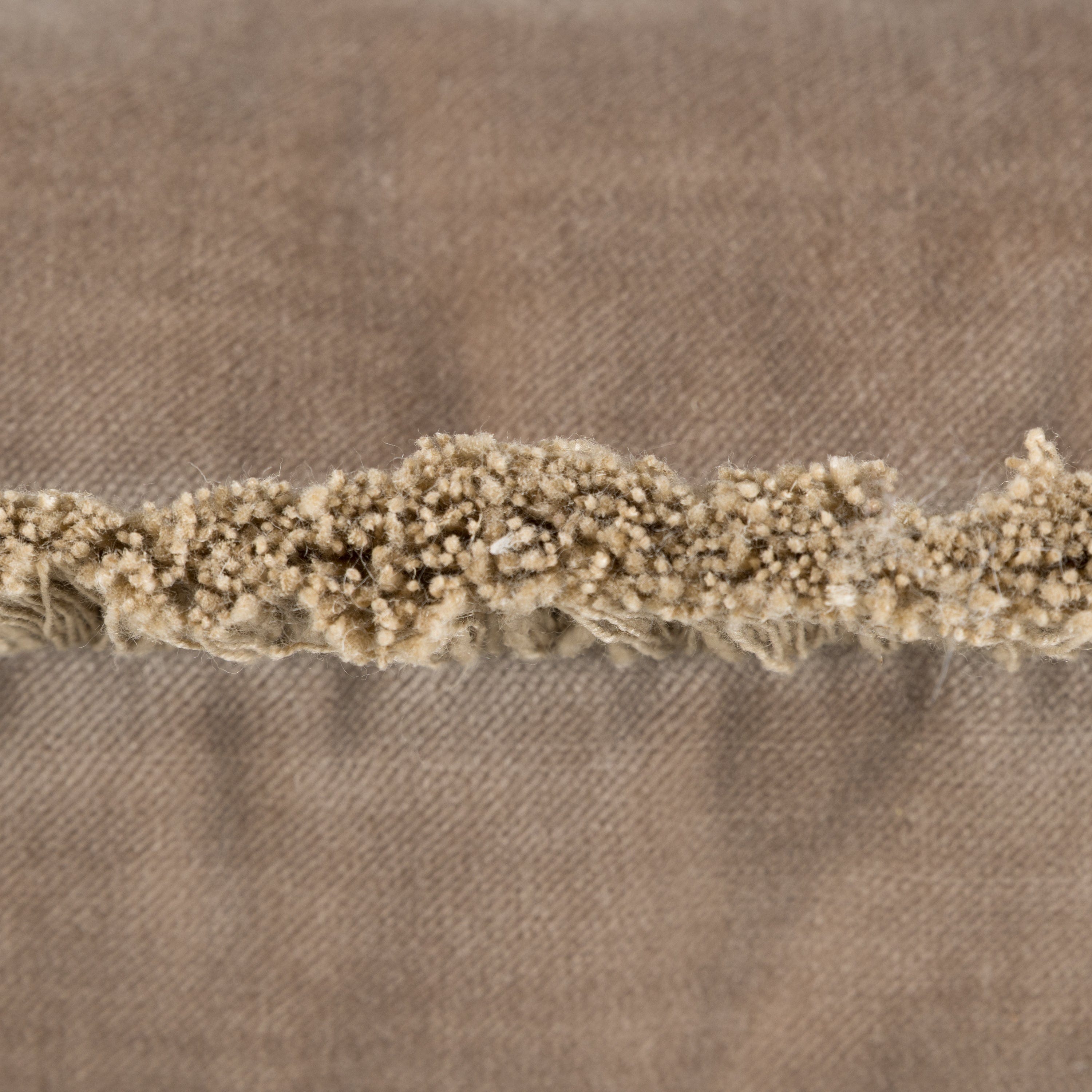 Close-up of a textured fabric with a frayed edge on a brown background