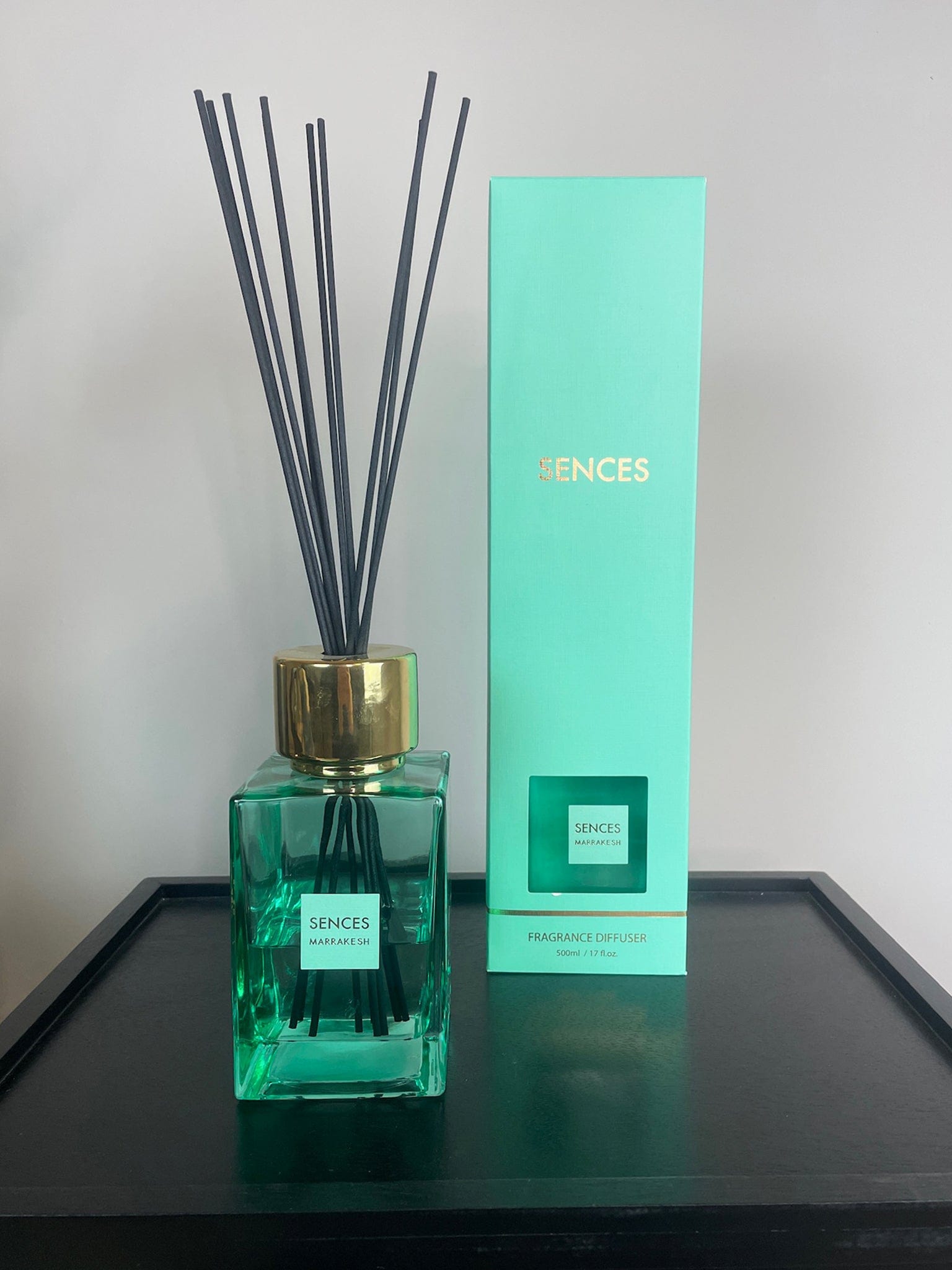 Green diffuser bottle with black sticks and matching box on a black shiny surface.