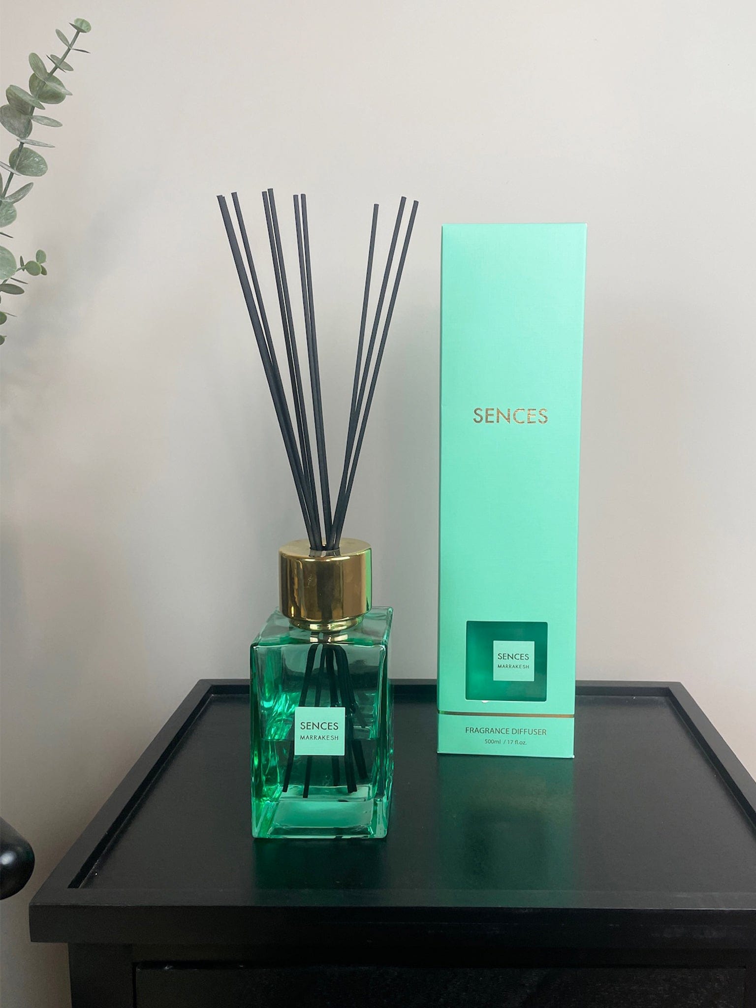 Green diffuser bottle with gold cap and black sticks on a black surface next to a green box labeled 'SENCES'.