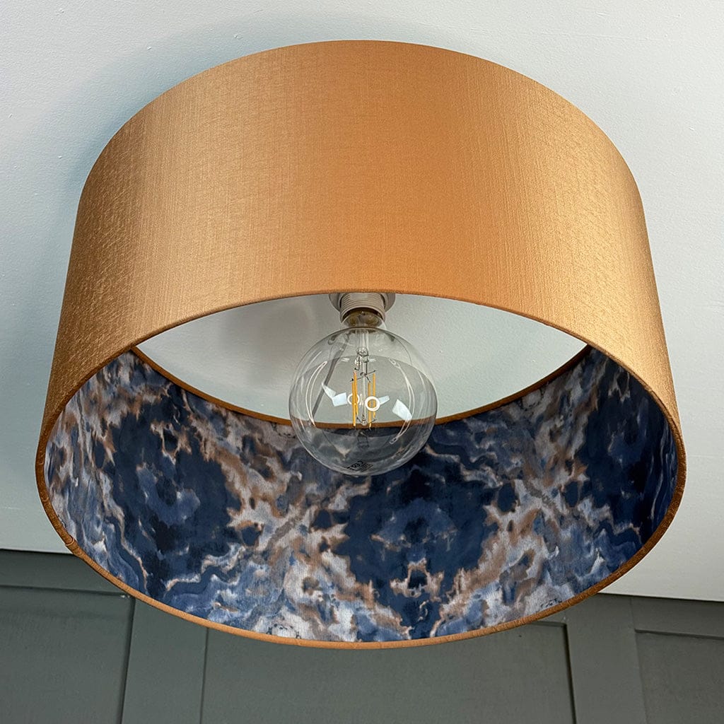 Lamp with a gold shade and blue marbled interior, featuring an exposed light bulb.