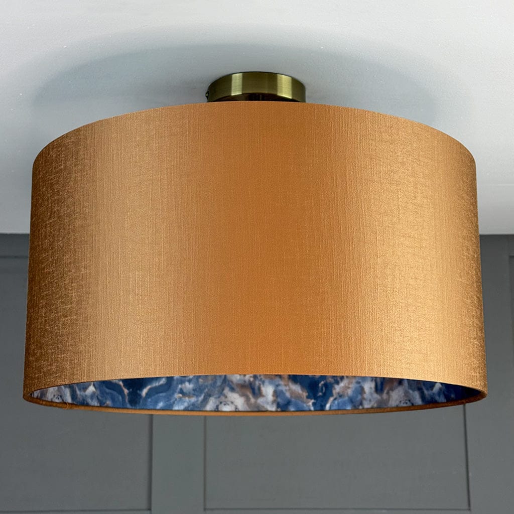 Ceiling light fixture with a gold shade and blue interior against a gray wall.