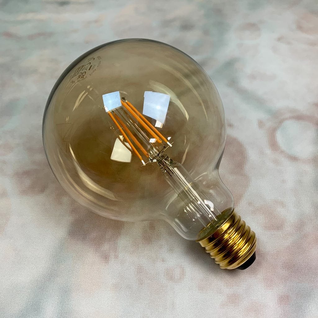 An E27 amber tinted LED globe light with a 125mm diameter and a 7.5W power rating, displayed against a marble background.