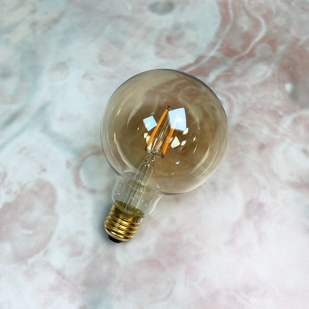 An amber tinted LED globe light bulb with a screw base, placed against a marble background.