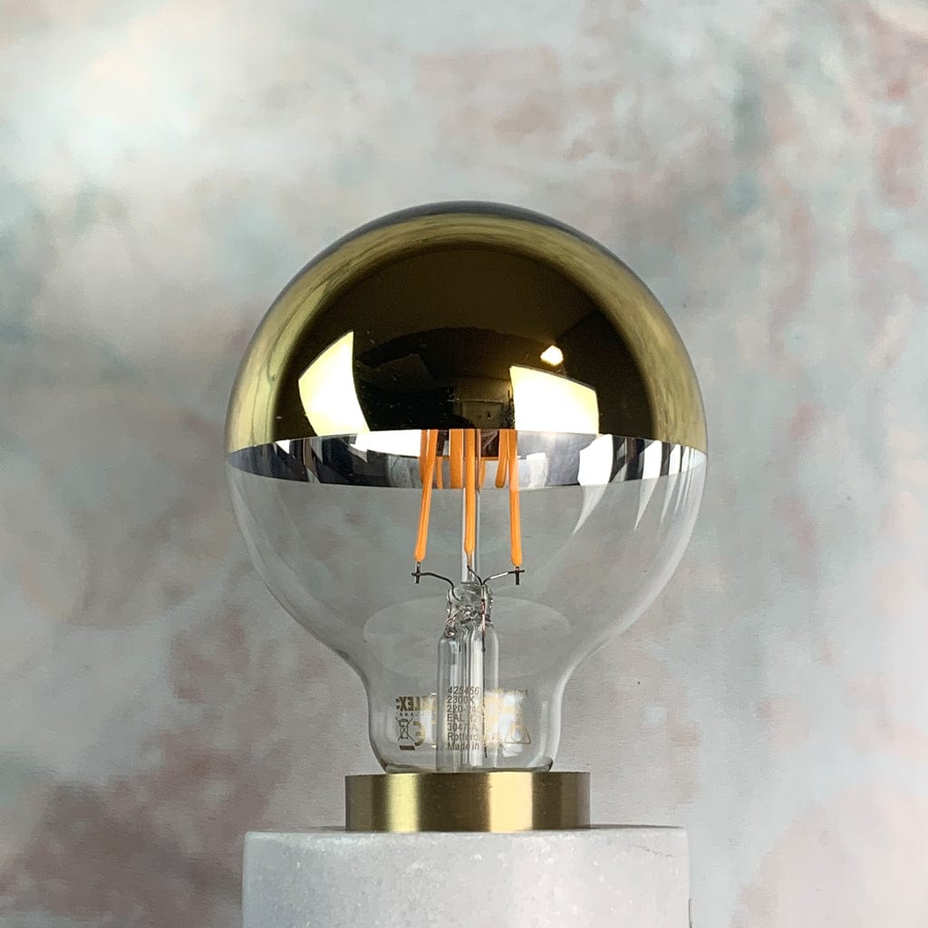 A dimmable LED light bulb with a gold top and clear glass bottom, designed for use in pendant shades. In a lamp holder