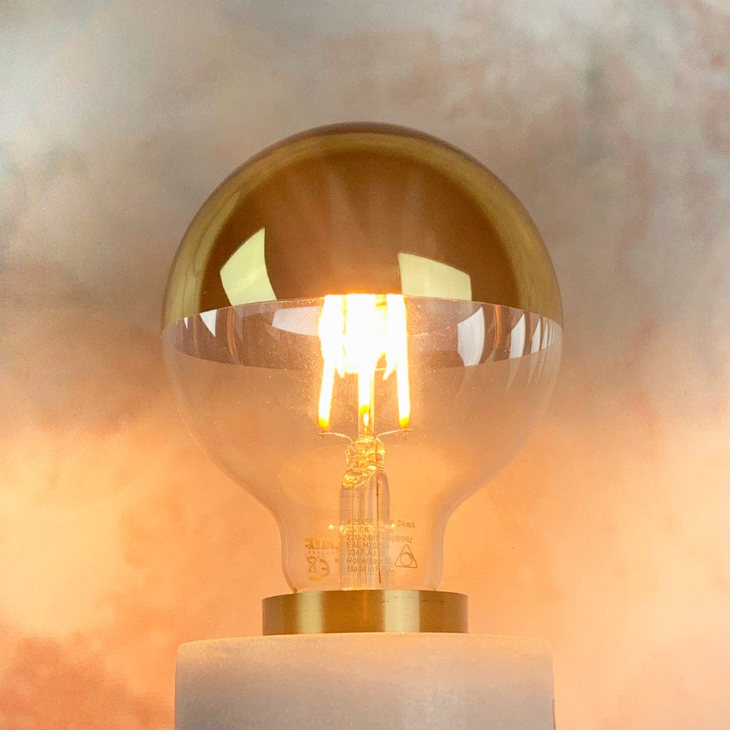 A dimmable LED light bulb with a gold top and clear glass bottom, designed for use in pendant shades. In a lampholder, lit