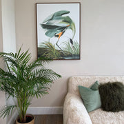 Living room with a framed artwork of a green and yellow crane in water, a plant, and a sofa with pillows.