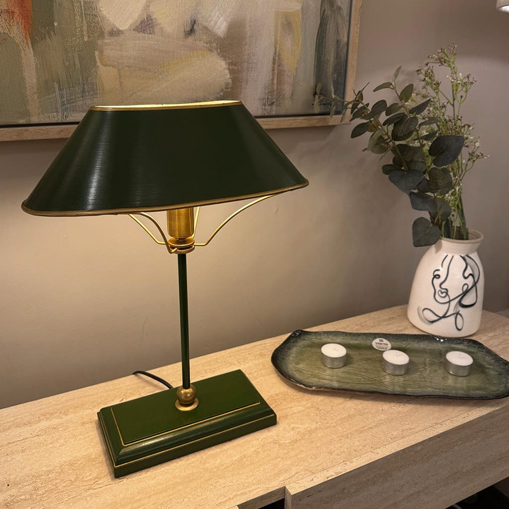 Green table lamp on a wooden surface with a vase of flowers in the background