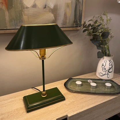 Green table lamp on a wooden surface with a vase of flowers in the background