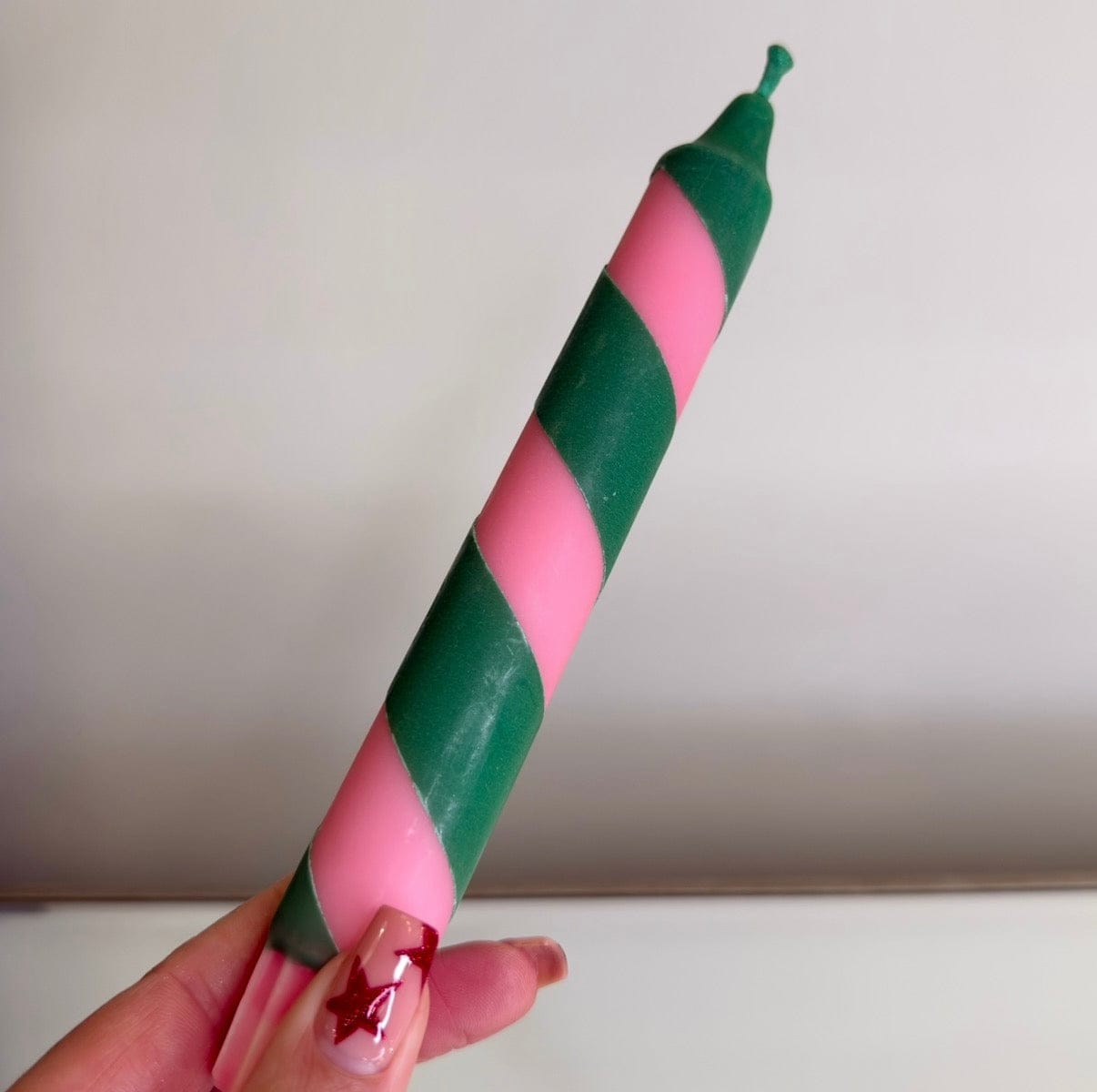 Pink and green striped candle held by a hand against a plain background