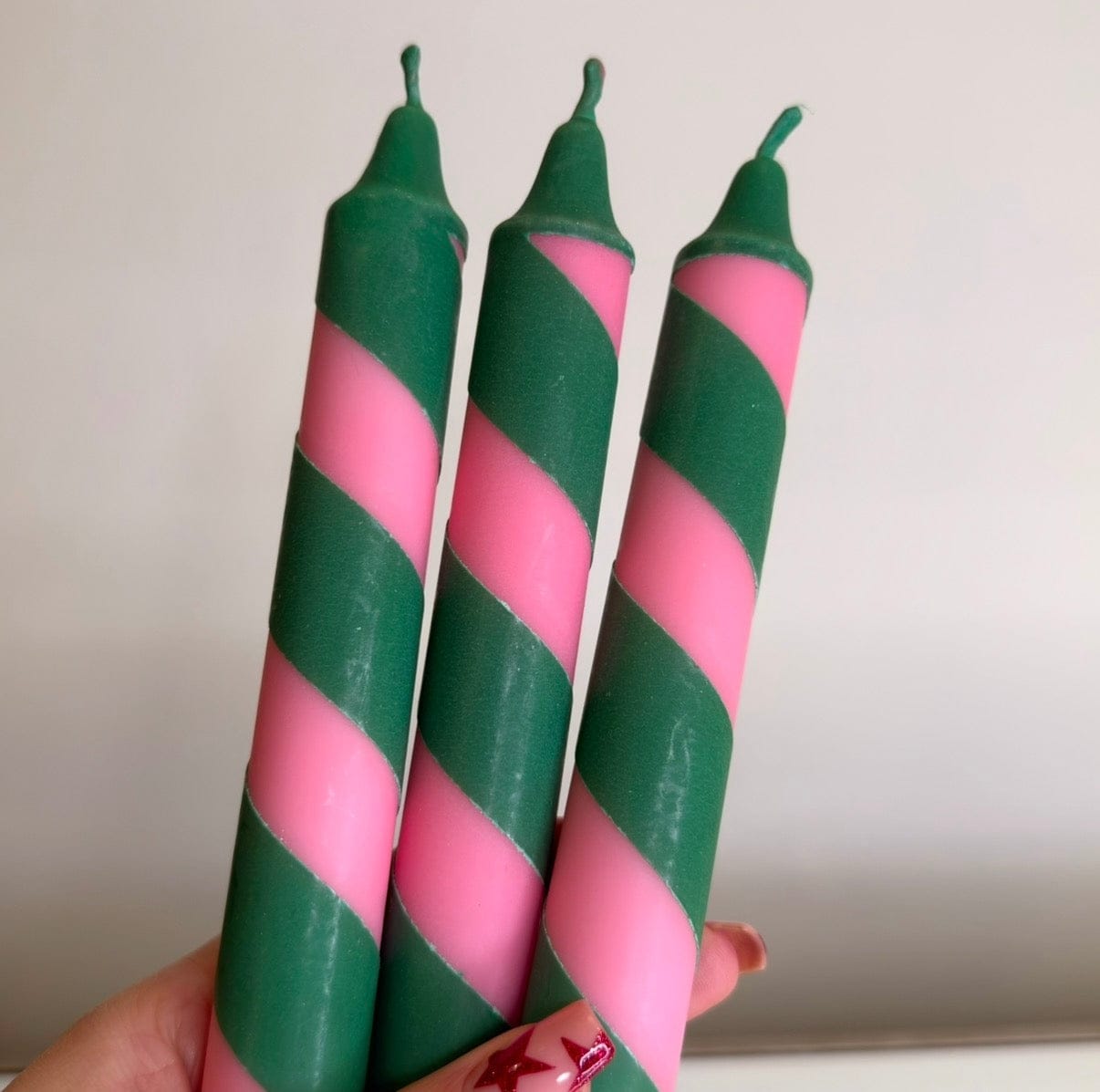 Three pink and green striped candles held against a plain background