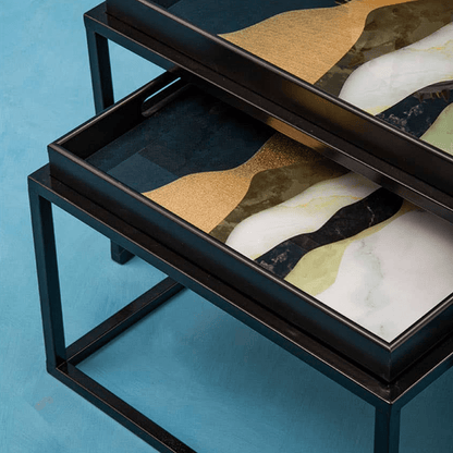 Two abstract art pieces on black metal frames against a blue background