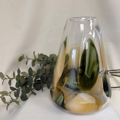 Glass vase with marbled design next to a branch of green leaves on a white background