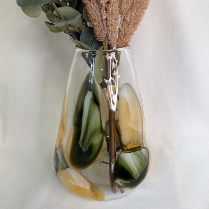 Decorative vase with green and brown tones holding dried plants on a light background