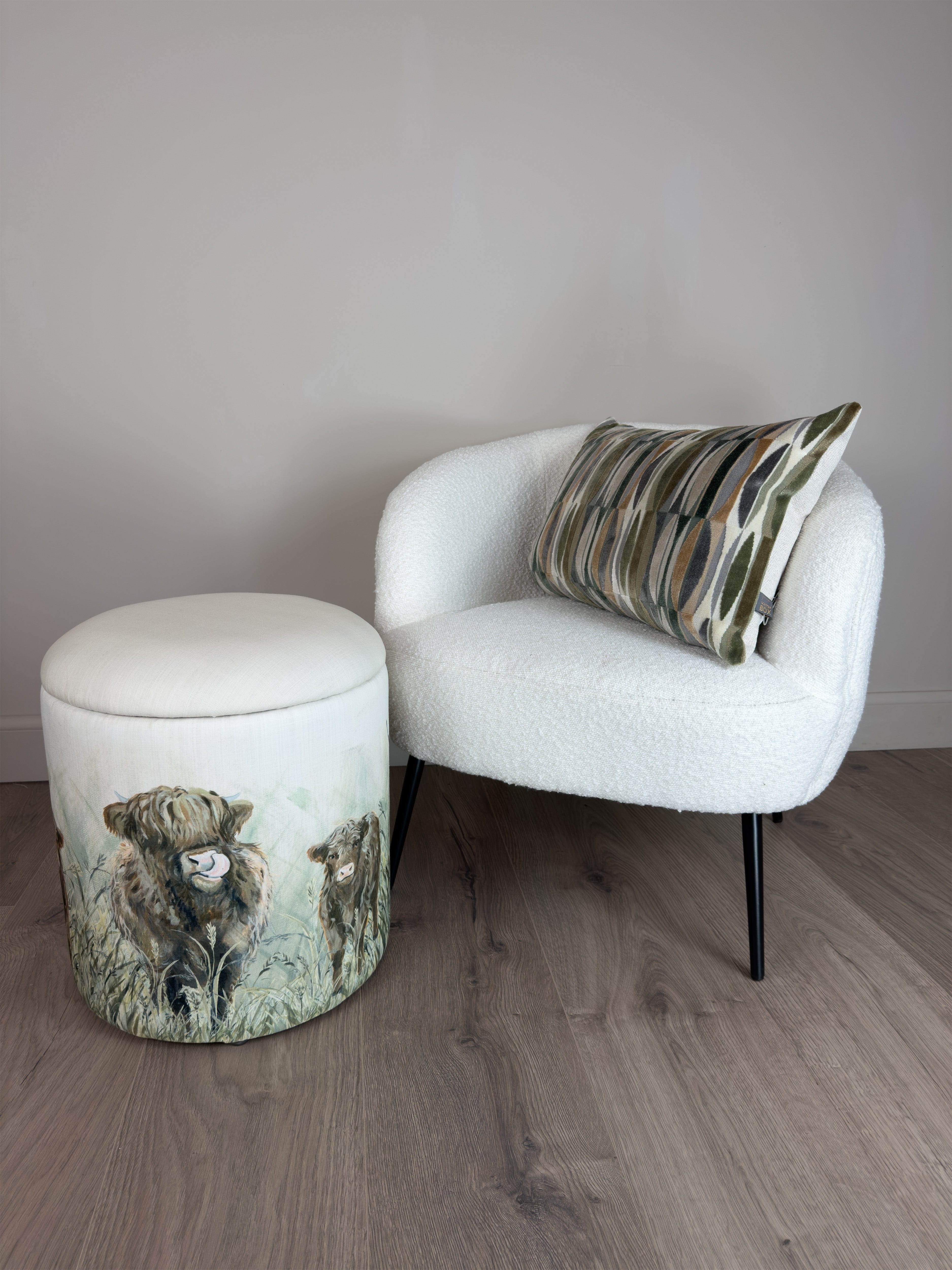 White armchair with a patterned pillow and matching ottoman with a highland cow design on a wooden floor.