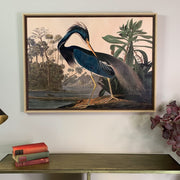 Framed artwork of a heron in a natural setting on a wall above a wooden console table.