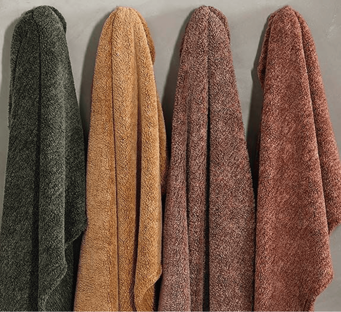 Four textured throws in green, beige, brown, and red on a neutral background