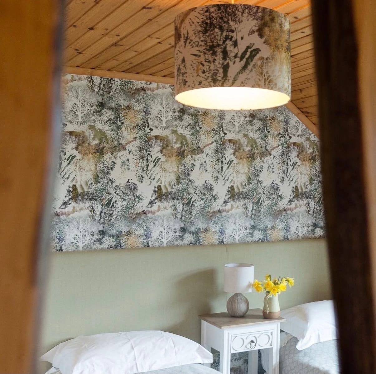 Room interior with floral wallpaper, lamp, and small table with flowers.