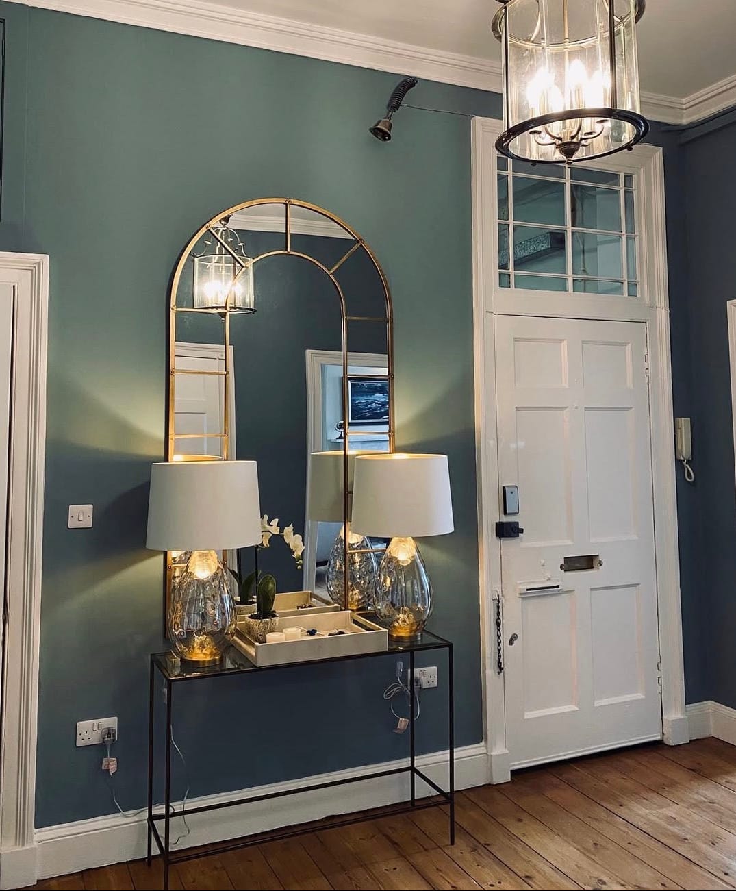 Decorative mirror and lamps in a room with a chandelier and door.