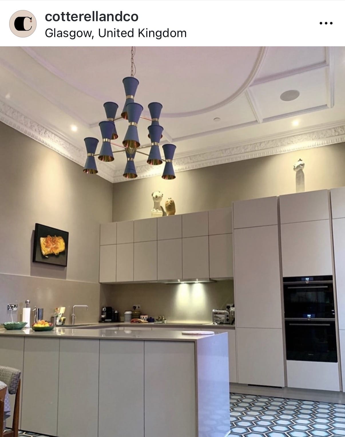 Modern kitchen with gray cabinets, a chandelier, and a TV mounted on the wall.