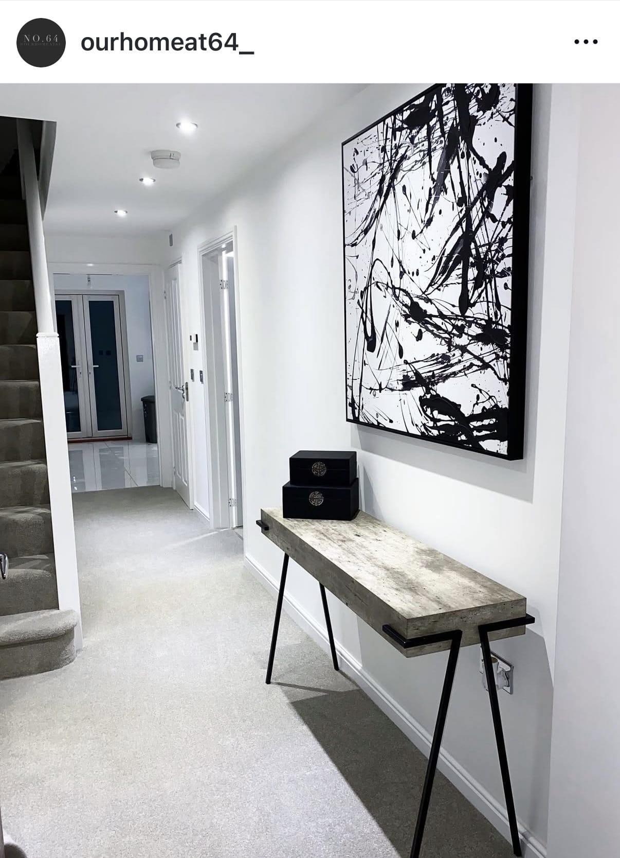Modern hallway with abstract black and white artwork on a white wall, featuring a wooden console table.