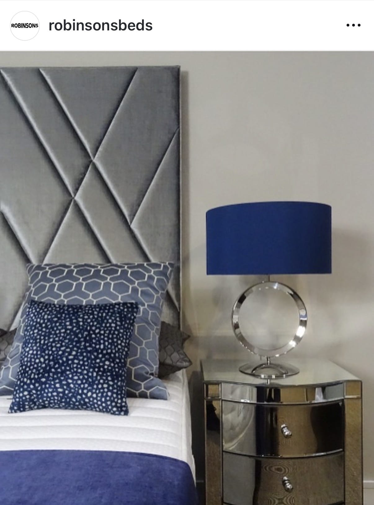 Bedroom setup with gray upholstered headboard, blue lamp, and decorative pillows on a bed.