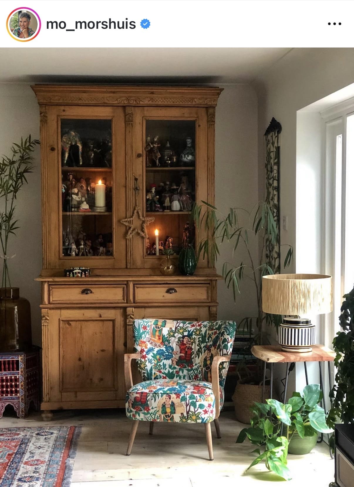 Wooden cabinet with decorative items in a room with a colorful armchair and plants.