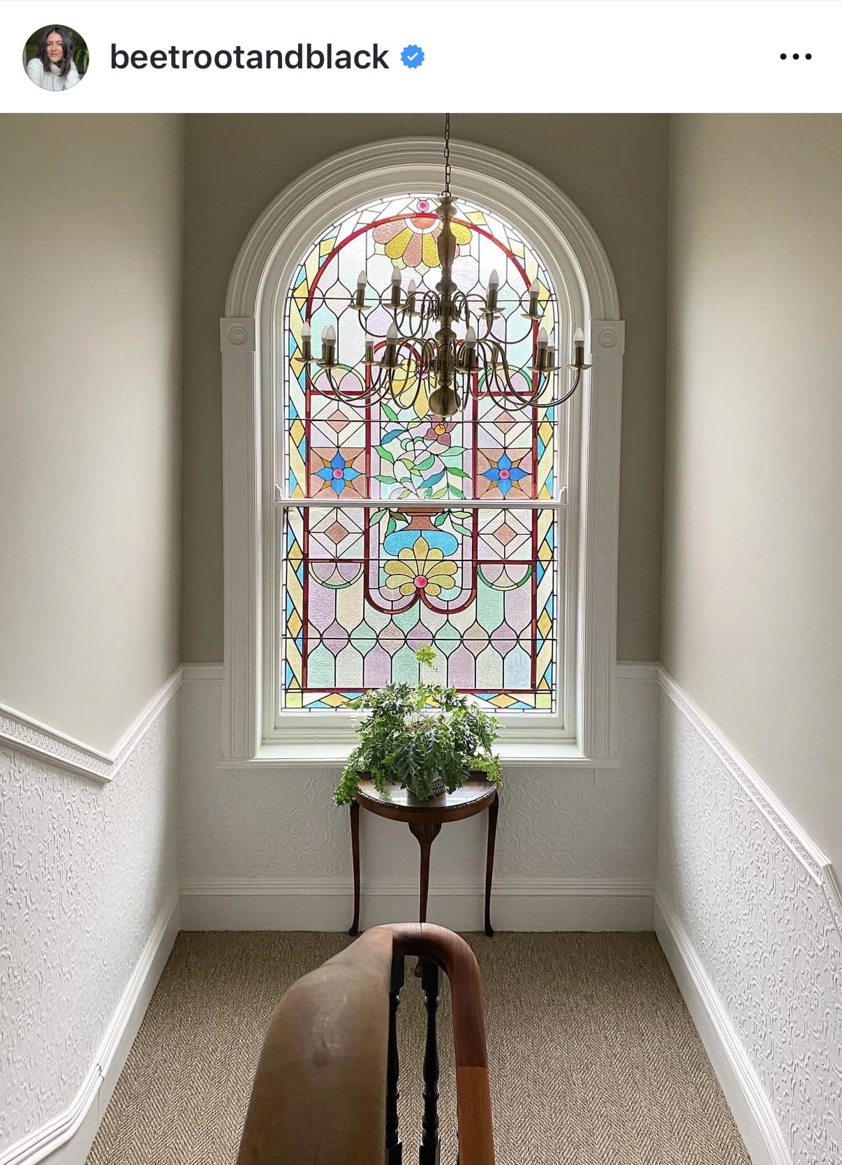 Stained glass window with colorful design in a room with a chandelier and plant.