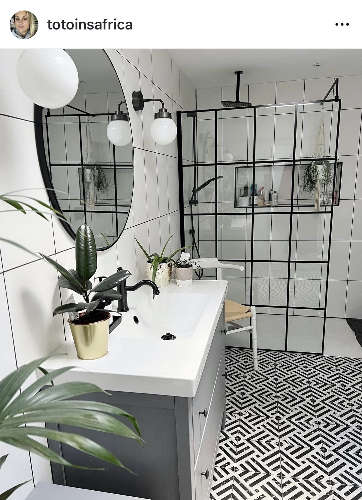 Modern bathroom with white tiles, black grid shower enclosure, and decorative plants.