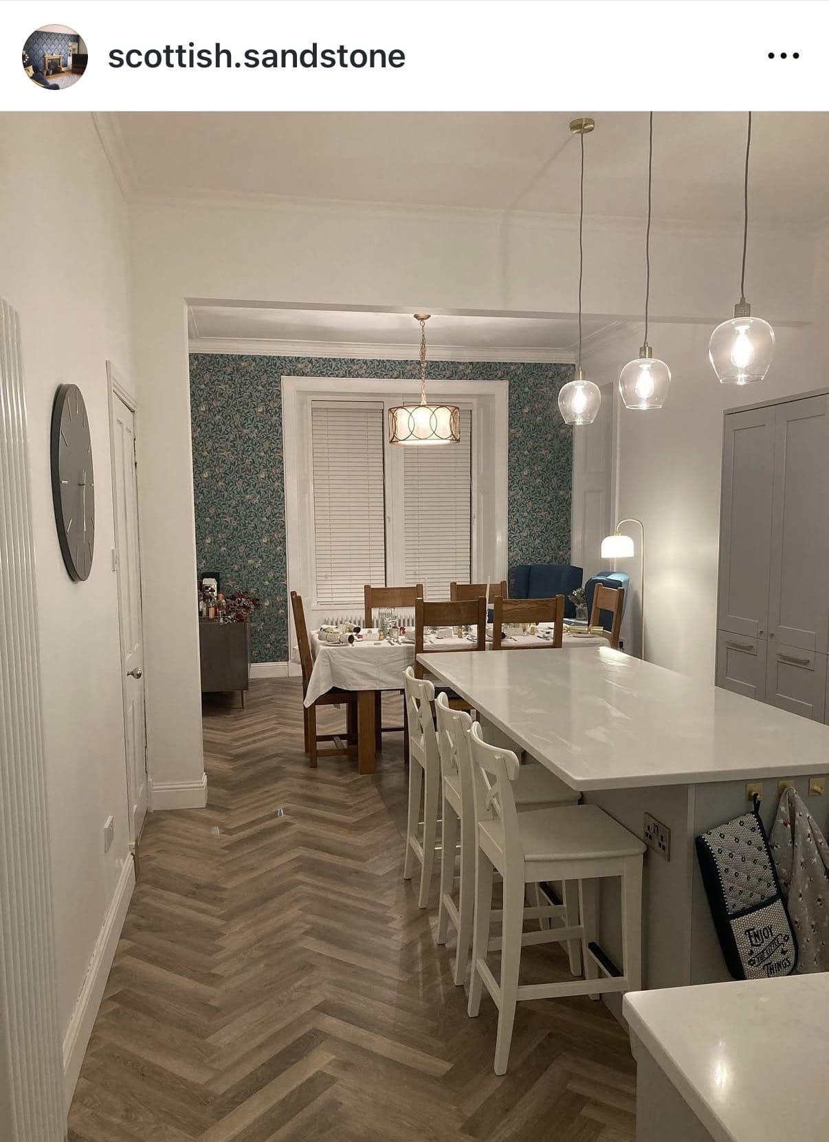 Modern kitchen with white countertops, wooden floor, and pendant lights.