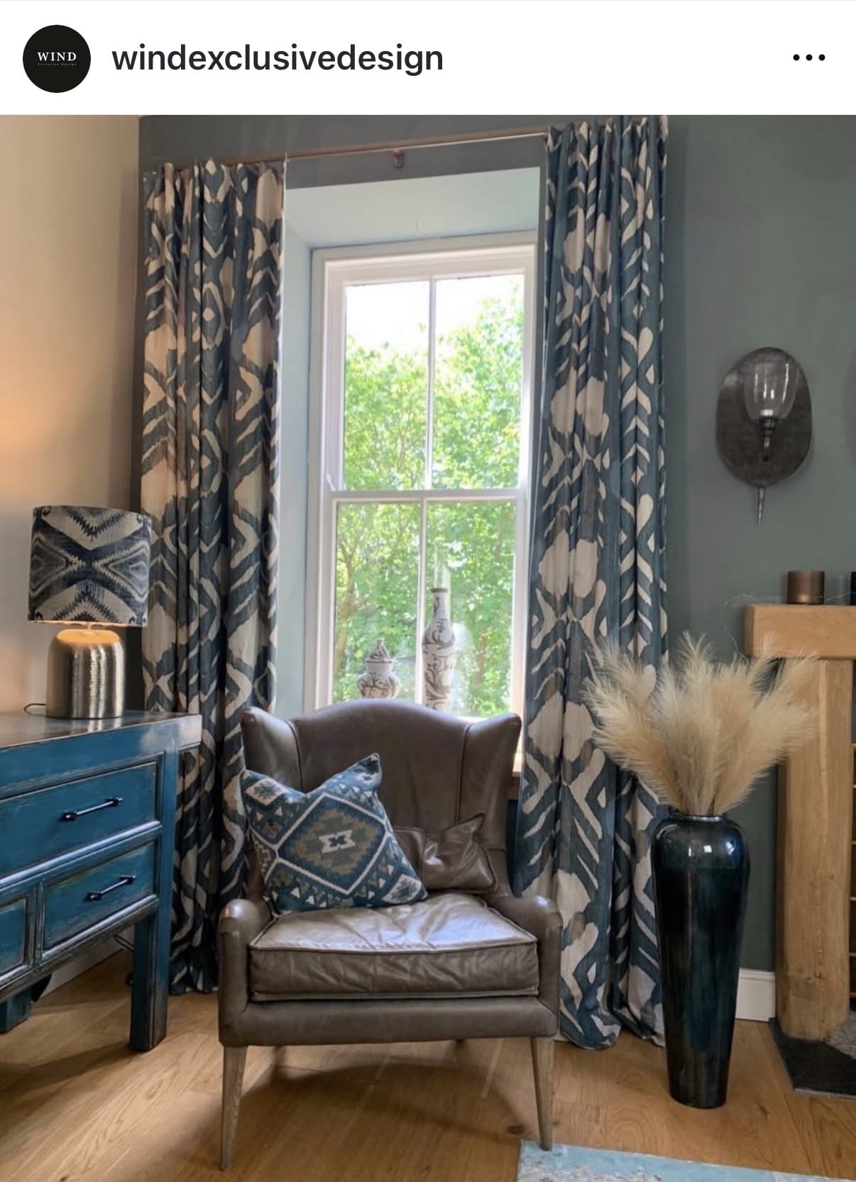 Living room with a brown armchair, blue side table, and patterned curtains.