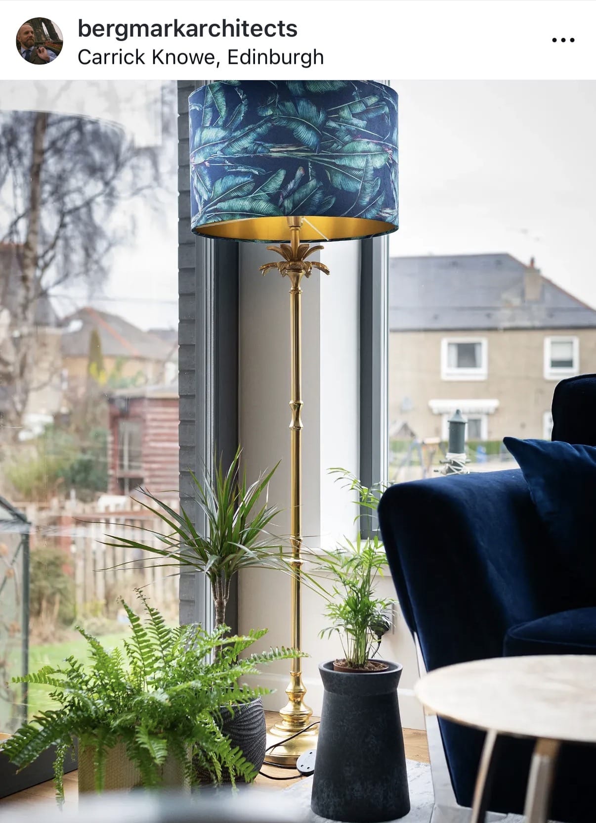 Futuristic lamp with a blue and gold design in a room with plants and a window view.