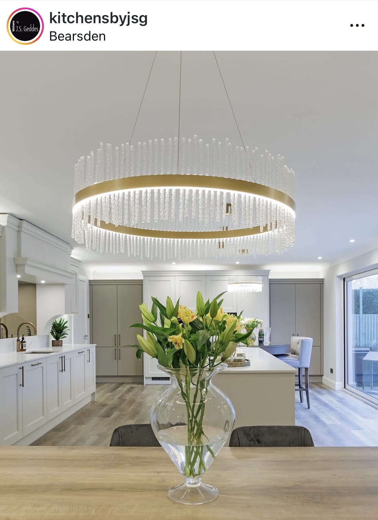 Modern kitchen with a large chandelier and a vase of flowers on a counter.