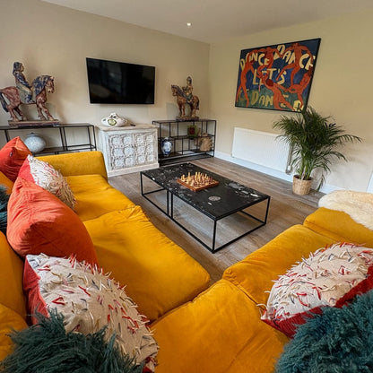 Living room with yellow sofa, colorful artwork, and decorative items.