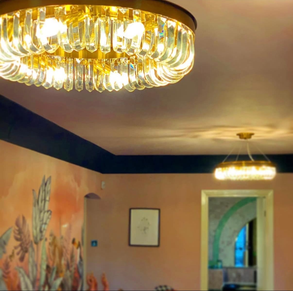 Gold chandelier hanging from a ceiling in a room with a painting on the wall.