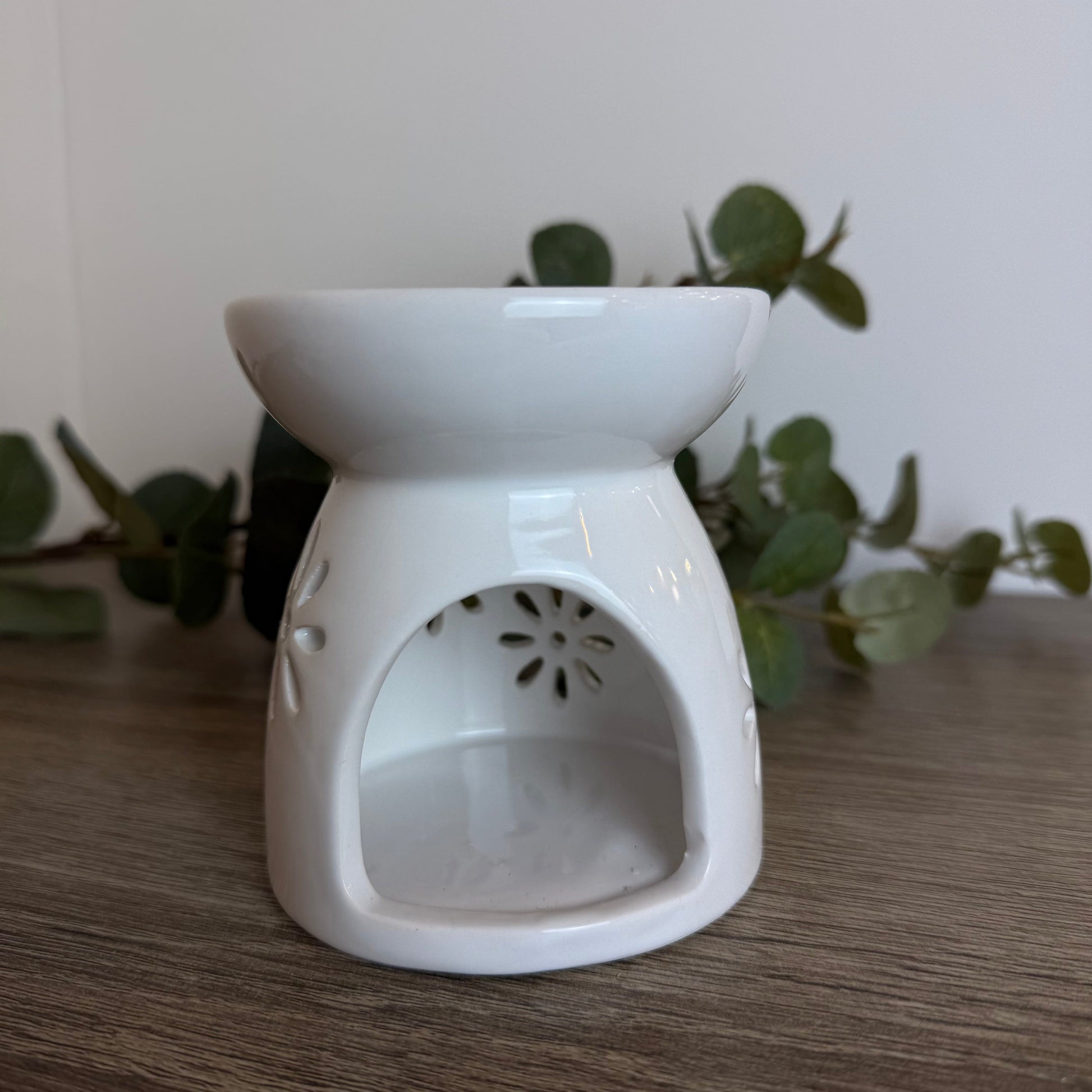 White ceramic oil burner on a wooden surface with green leaves in the background