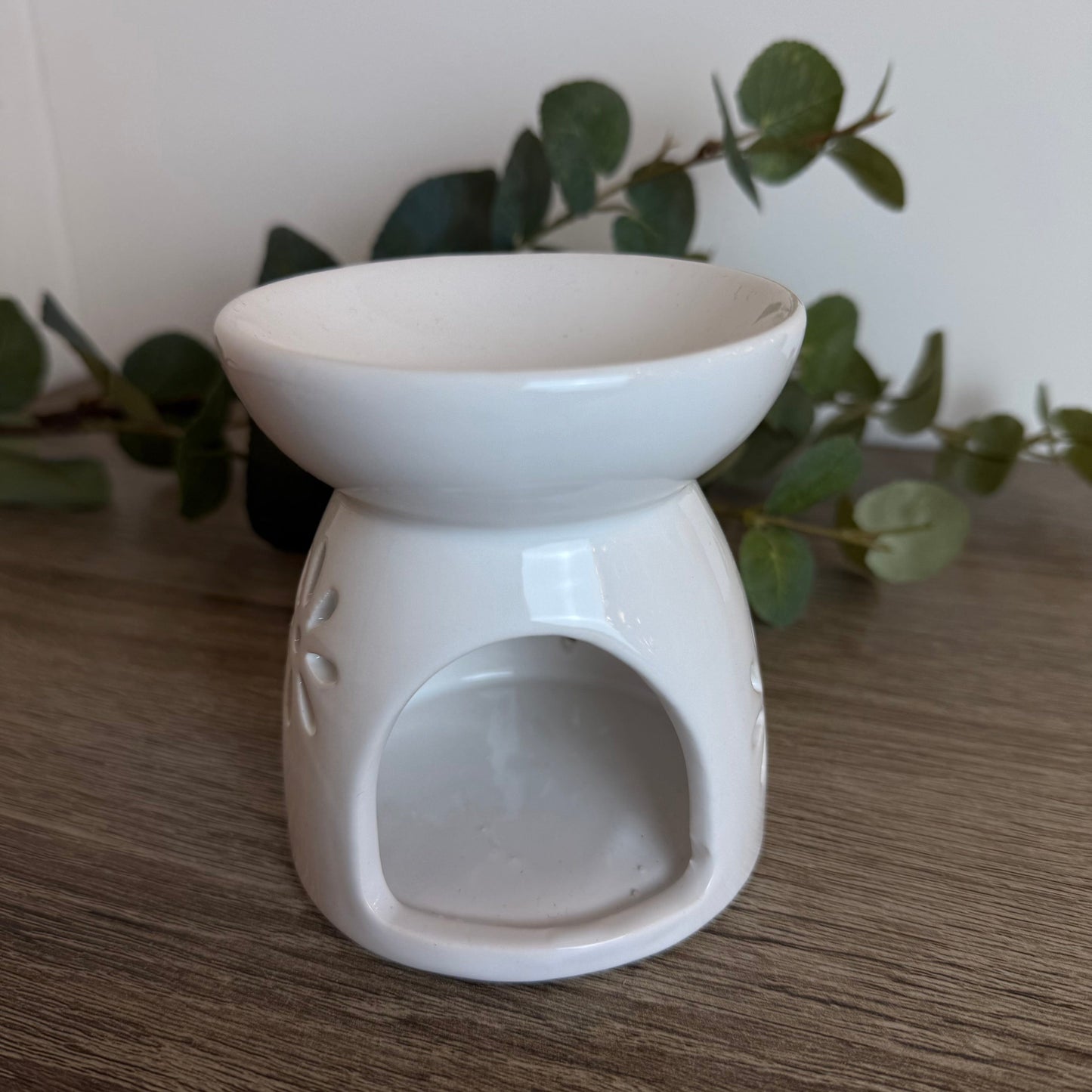 White ceramic oil burner on a wooden surface with green leaves in the background