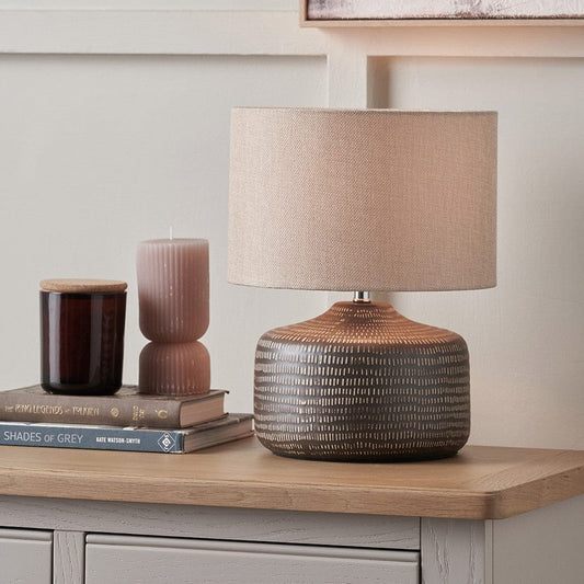 Decorative lamp with textured base and beige shade on a wooden surface.