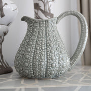 A large grey jug with a textured surface, resembling the shape of a sea urchin, placed on a table.