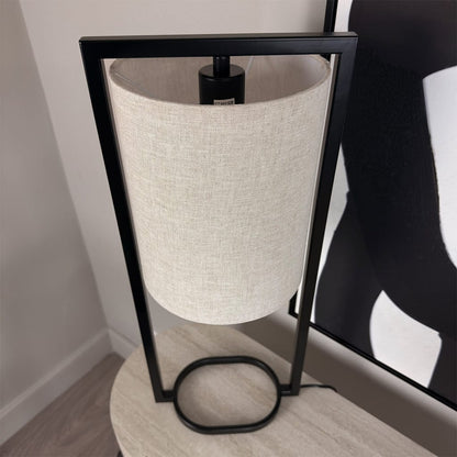 Table lamp with black frame and white lampshade on a wooden surface.