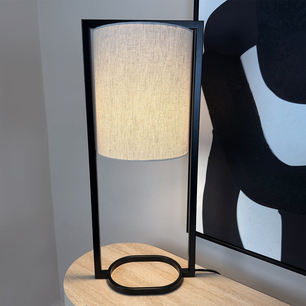 Table lamp with a black frame and beige shade on a wooden surface.