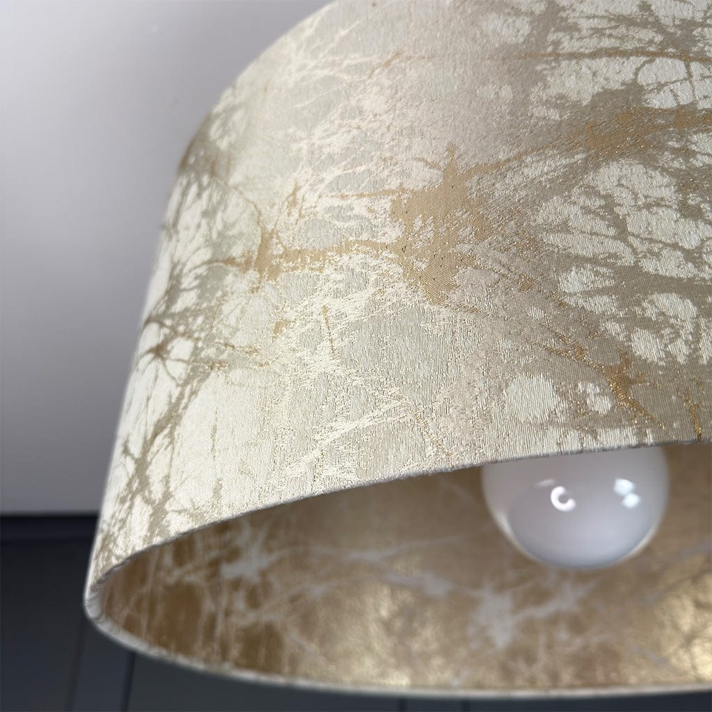 Close-up of a textured beige/gold/cream lampshade with a light bulb inside.