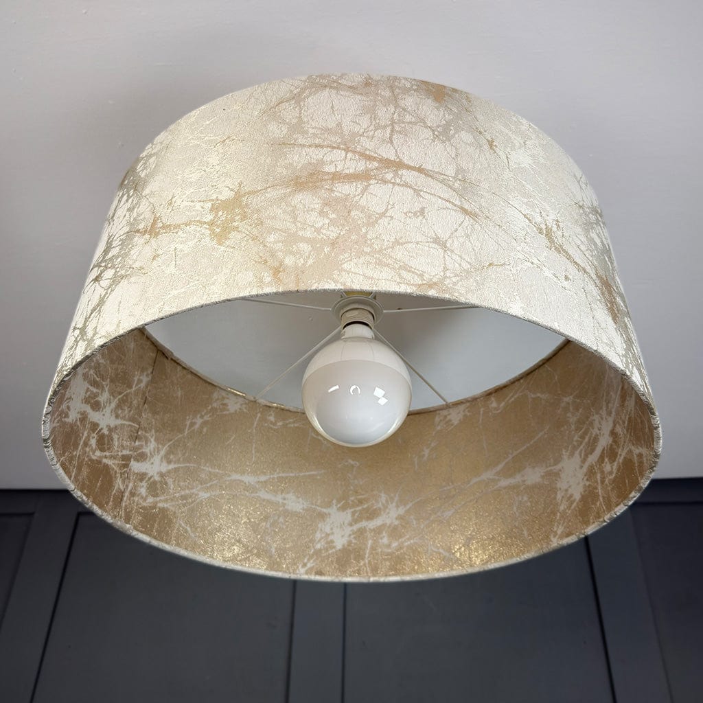 Lamp with a textured cream gold and beige shade and white bulb on a dark surface.