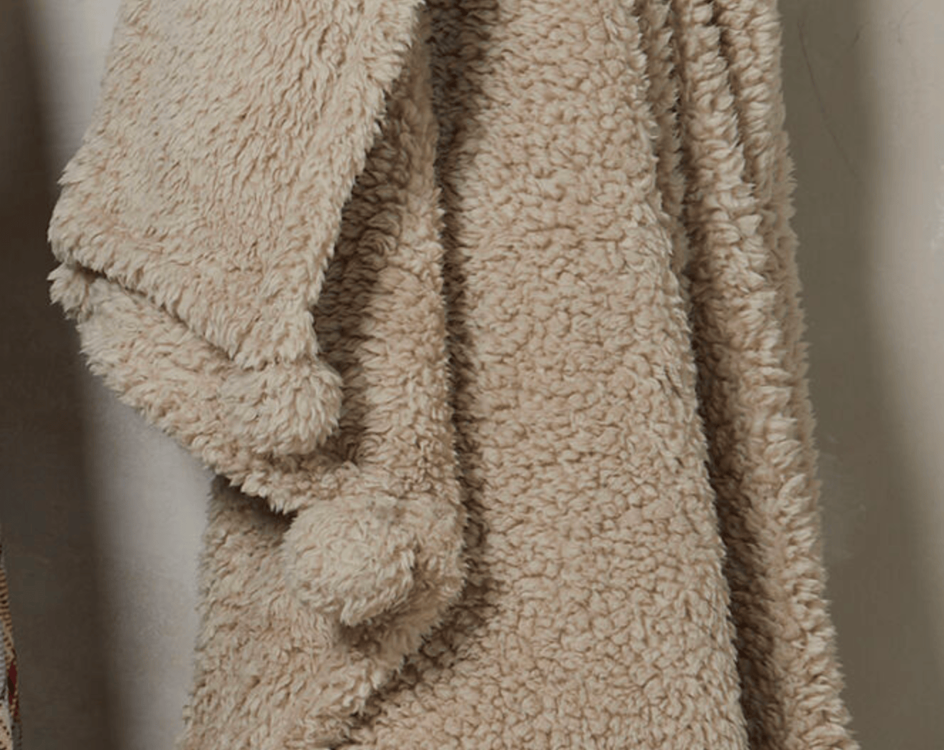 Beige fluffy blanket draped over a surface with a neutral background