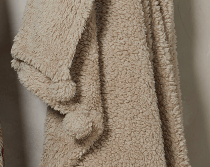 Beige fluffy blanket draped over a surface with a neutral background