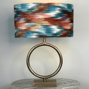 Table lamp with a colorful abstract shade and gold base on a gray surface.