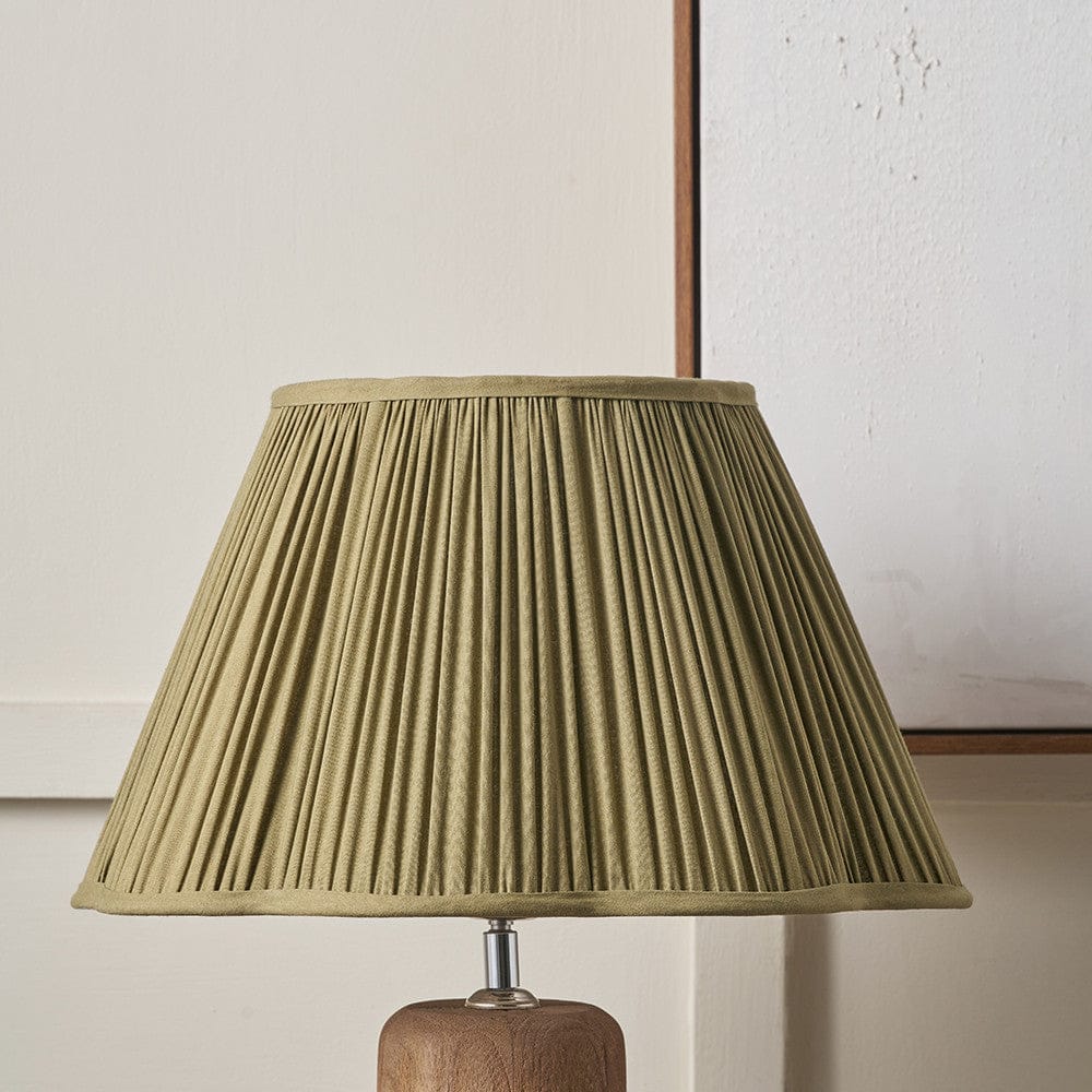 Lamp with a pleated green shade on a wooden base against a neutral wall.