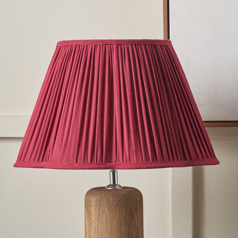 Lamp with a pleated red shade and wooden base on a neutral background