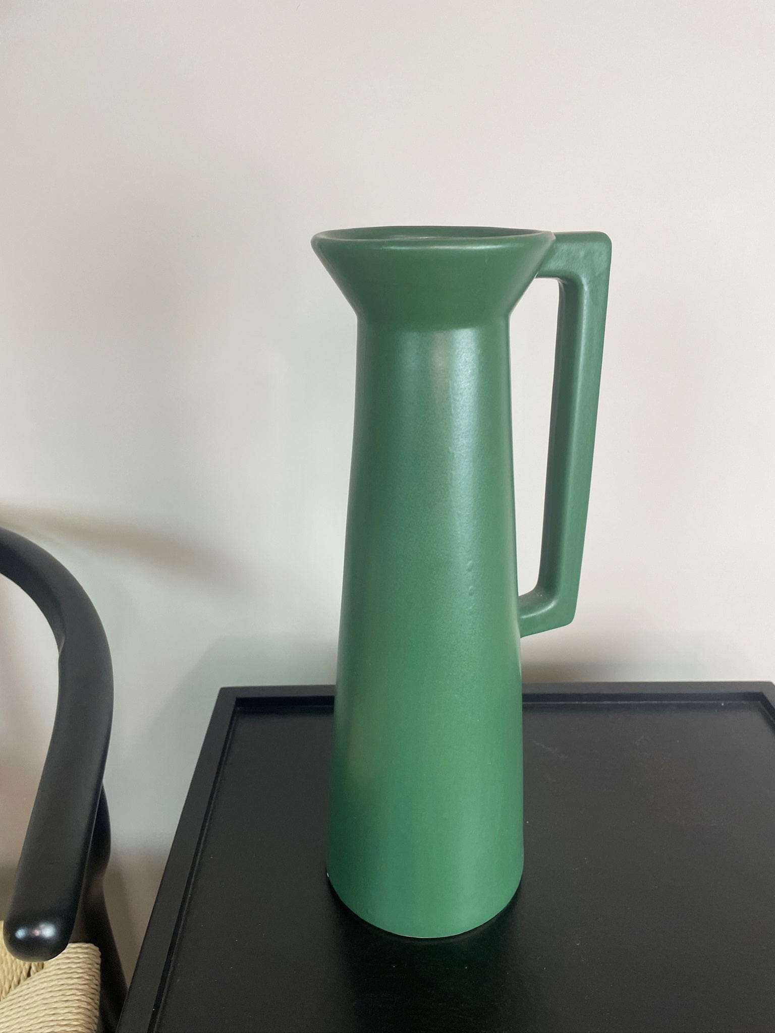 Green pitcher on a black surface with a white background